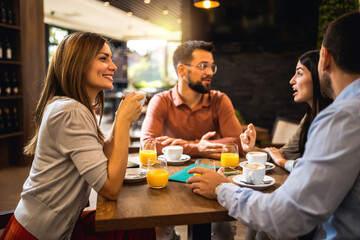 Friends chilling at the cafe. They are drinking coffee and orange juice while they talk and hang out.