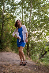 Slim young woman posing in the forest in a tight blue mini dress