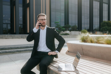 Young Businessman in Suit and Glasses Talking on Phone Outside Office Building