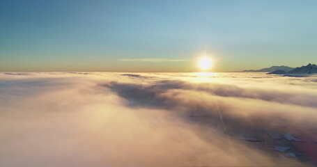 Aerial high angle flight over morning colorful cloudscape. Sunrise sun shine bright layers of fluffy clouds, arctic ocean water and mountain range peaks. Nature background perfect landscape wallpaper