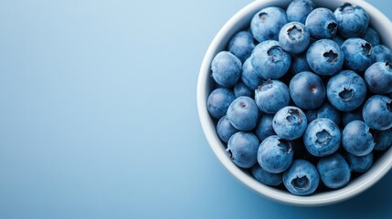 A cluster of plump blueberries fill a white ceramic bowl, capturing the essence of freshness and health, with their vibrant blue color beautifully striking against the pale dish.