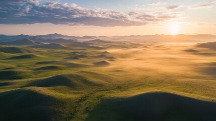 As dawn breaks, the sun casts a warm glow over rolling green hills, revealing a misty valley that enhances the tranquil beauty of the countryside