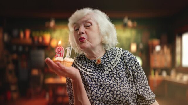Glad elderly woman blowing out candles on birthday cake, age is just a number