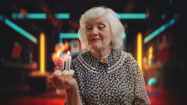 Smiling granny blowing out candles on birthday cake against cafe background
