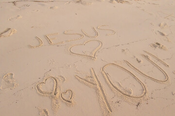 Jesus loves you written in the sand at a beach 