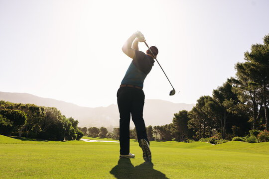 Golfer swinging a golf club with powerful follow-through on a sunny fairway - Powered by Adobe