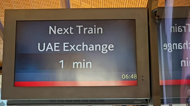 A digital display at a train station shows "Next Train UAE Exchange 1 min at dubai rta metro station and the time reflecting the platform environment.
