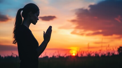 Fototapeta premium A silhouette of a woman praying at sunset, surrounded by nature's beauty.
