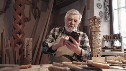 Caucasian male sitting behind table in working area and using mobile device. Tapping on screen. Opening something or searching in smartphone. Finding difficult to use modern technology. - Powered by Adobe