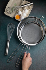 Eggs, whisk and kitchen utensils on dark background