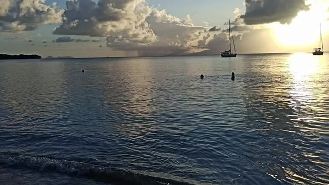 Sunset view from Anse Canot beach in Marie Galante with swimmers in caribbean sea and sailboats in the evening sunlight, hd video