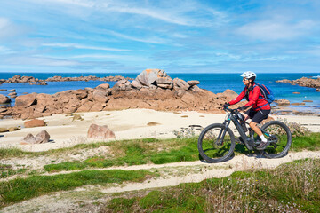 nice senior woman cycling with her electric mountain bike at the rocky rose granite coast  at...
