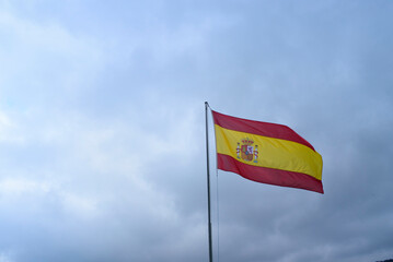 Bandera de España ondeando al viento en mástil sobre cielo nublado