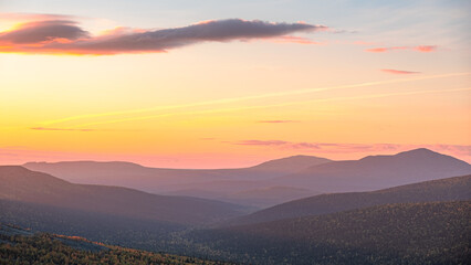 Tranquil mountain landscape at sunset, showcasing rolling hills under a pastel sky with soft orange and pink hues. 