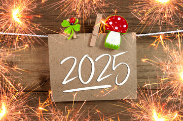 Wooden hang tag and slate with four leaf clover and sparklers with the german words for happy new year - frohes neues jahr 2025 on wooden weathered background
