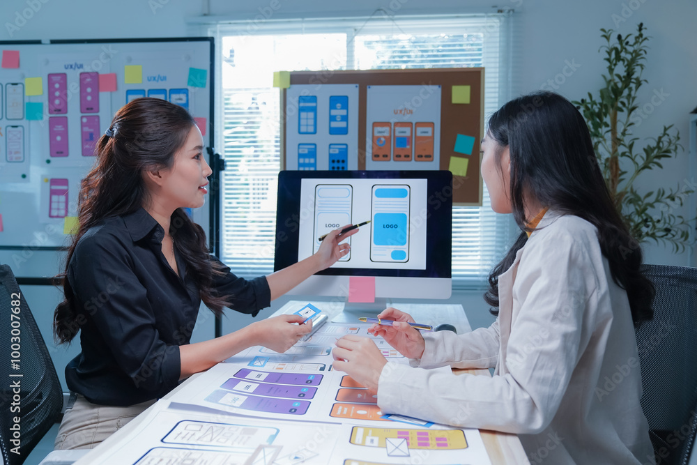 Wall mural two women are working together to design a mobile application for smartphones, using wireframes and 