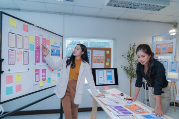 Two asian ui/ux web designers are discussing the user interface on a mobile application wireframe...
