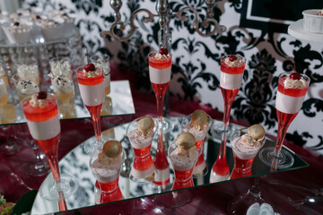 A table with a variety of desserts, including a tray of pink and white desserts and a tray of red and white desserts
