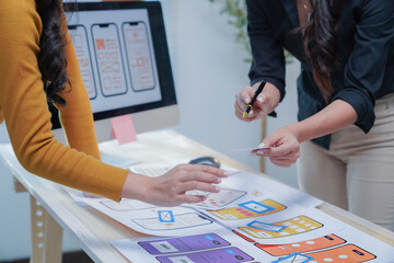 Two female designers collaborate on a mobile app wireframe in a modern office, brainstorming and analyzing ideas for their project