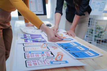 Two female ui/ux designers are working together, arranging mobile application wireframes on a desk....