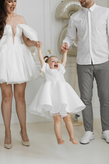 Smiling young girl in white dress lifted by diverse parents. Joyful moment captured in elegant...