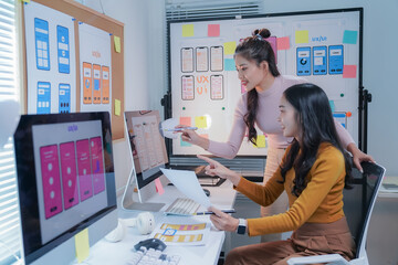 Two female ui and ux designers are working together in the office, discussing over new mobile...