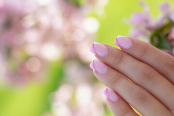 Beautiful female hand with pink manicure nails on flower background