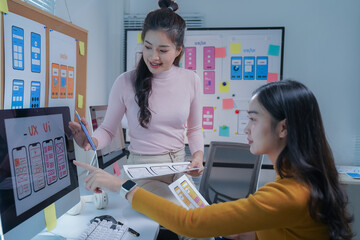 Two asian ui/ux web designers are working together in the office, discussing mobile app interface...
