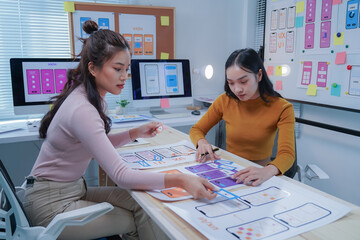 Two female ui/ux designers are working together to develop a mobile application, placing ui...