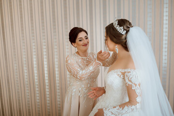 A bride is getting ready for her wedding with her mother helping her. The bride is wearing a white...