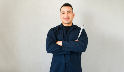 Confident young mechanic smiling and holding a wrench in front of a gray backdrop