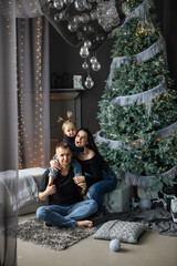 Naklejka premium Cheerful Caucasian family with parents and young daughter enjoying Christmas at home. Cozy living room setting with decorated Christmas tree, presents, and festive lights.