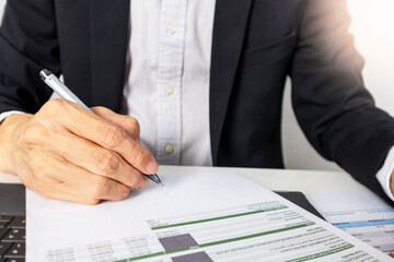 A businessman in a black suit is signing financial records, a company plan, and a contract.