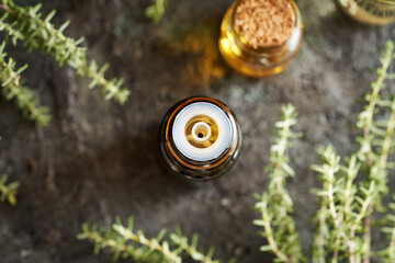 A brown dropper bottle of aromatherapy essential oil with fresh thyme leaves, top view