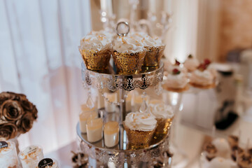 A table with a stack of cupcakes and a ring on top. The table also has other desserts and a vase