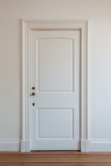 A simple white door framed by classic molding in a minimalistic room with wooden flooring