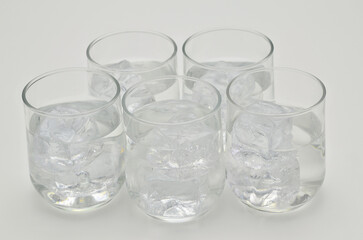 Five glasses of water with ice cubes, close up, isolated on white background
