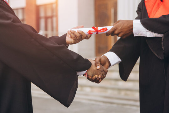 Graduation Ceremony Handshake with Diploma Exchange Between Two Individuals in Academic Gowns Celebrating Achievement