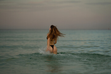 Summer girl running and splashing in sea water. Outdoor fashion portrait of sexy fit tan perfect woman in sexy bikini swim in the sea. Summer mood. Beach trendy swimsuit. Sexy body.