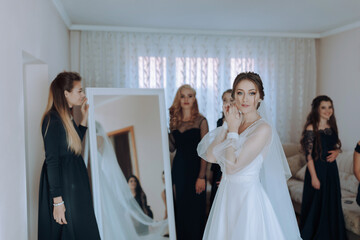A bride is getting ready for her wedding with her bridesmaids. She is standing in front of a...