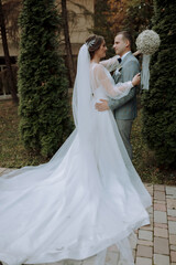 A bride and groom are standing in front of a bush, with the bride wearing a white dress and the groom wearing a blue suit