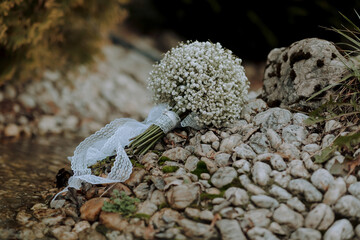 A bouquet of white flowers is on a rocky surface. The flowers are arranged in a vase and are surrounded by rocks. The scene has a natural and rustic feel to it