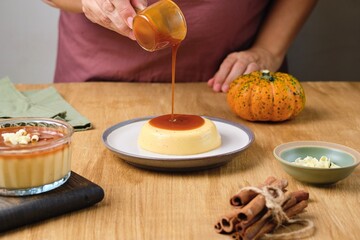 Woman pouring caramel sauce over pumpkin panna cotta on white dessert plate on wooden background. Desserts without baking. Pumpkin recipes. Thanksgiving Day.