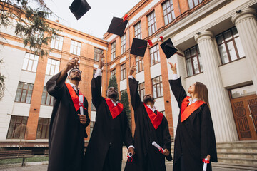 Joyful Graduates Celebrating In Front of University Building, Tossing Caps In the Air