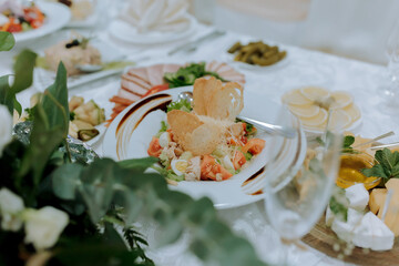 A white plate with a salad and a glass of wine. The salad is topped with bread crumbs and has a variety of vegetables, including tomatoes and cucumbers. The wine glass is filled with a clear liquid