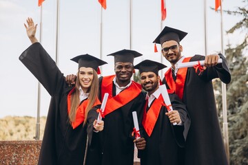 Joyful Group of Graduates Celebrating Achievement in Academic Robes Holding Diplomas Outdoors