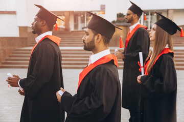 Group of Diverse Graduates in Caps and Gowns Celebrating Graduation Day Outdoors
