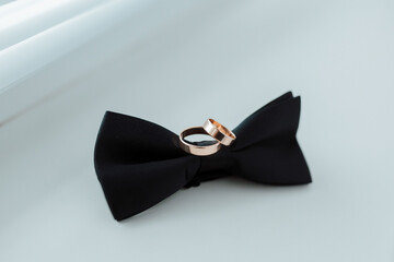 Two rings are on a black bow tie. The rings are gold and are placed on top of each other