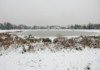 Snow covered ground and frozen lake in a London park
