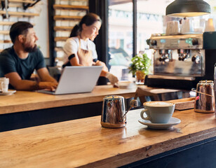 Fototapeta premium -A cozy coffee shop interior with wooden tables, soft lighting, and customers working on lap